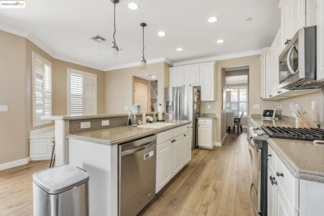 a kitchen with stainless steel appliances kitchen island granite countertop a stove a sink a refrigerator and white cabinets with wooden floor