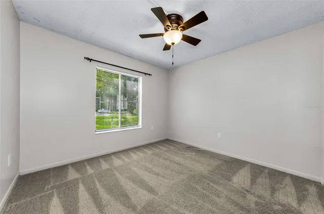 an empty room with chandelier fan and windows