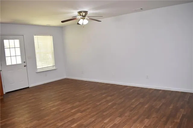 an empty room with wooden floor chandelier fan and windows