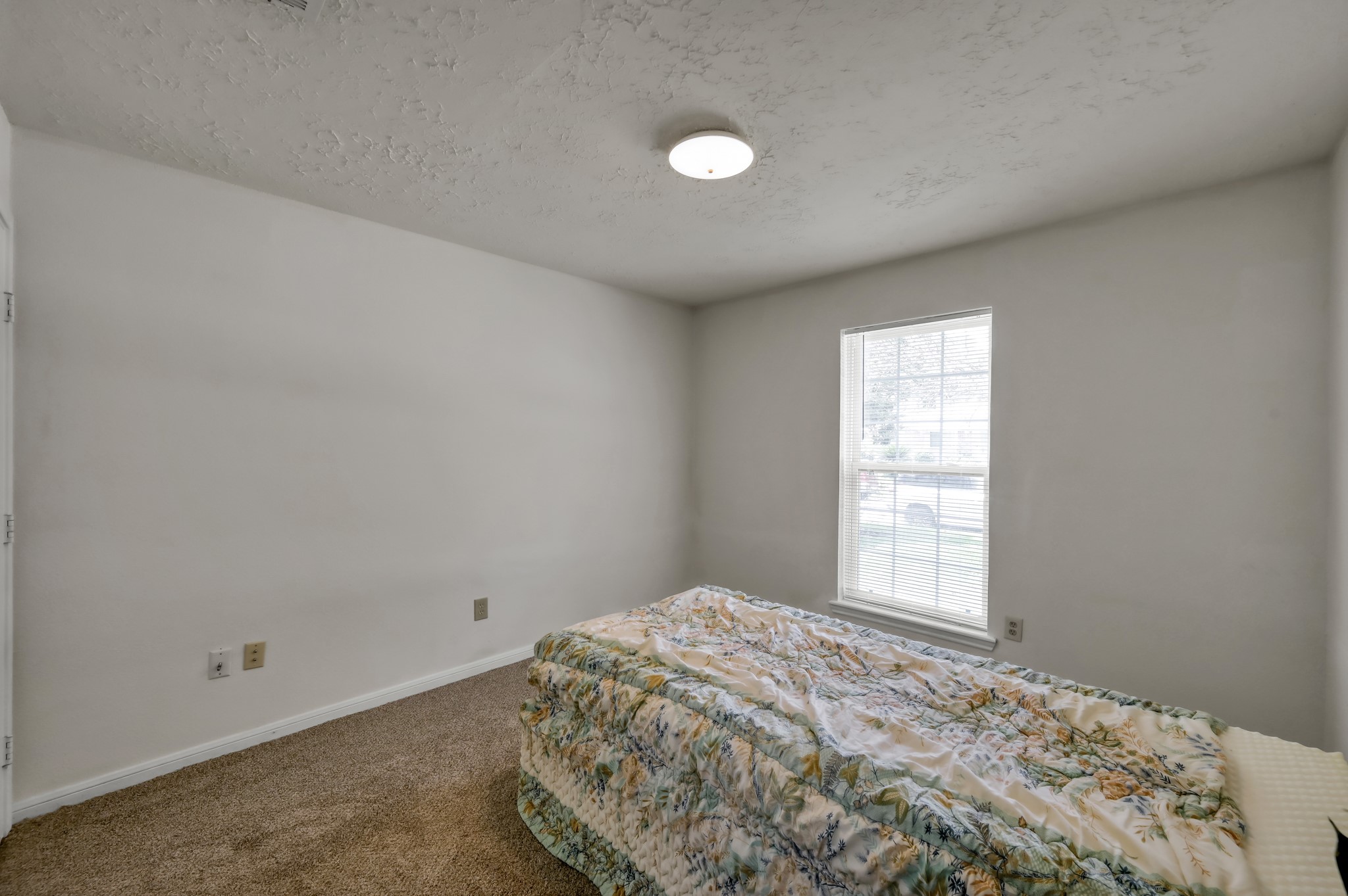 4314 Enchantedgate Drive Spring, TX 77373 - Photo 28 of 47 Guest bedroom features neutral walls, a textured ceiling with a modern light fixture, and a window that provides natural light. It's carpeted, creating a cozy atmosphere.