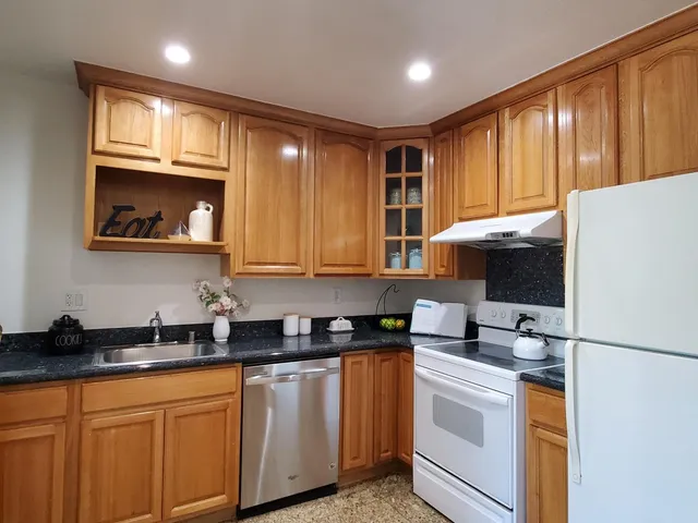 a kitchen with stainless steel appliances granite countertop a sink a stove a refrigerator with grey cabinets and wooden floor