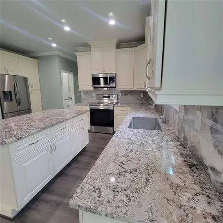 a large white kitchen with stainless steel appliances kitchen island granite countertop a sink stove and cabinets