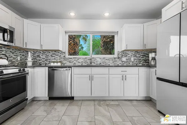 a kitchen with granite countertop white cabinets stainless steel appliances a sink and a window