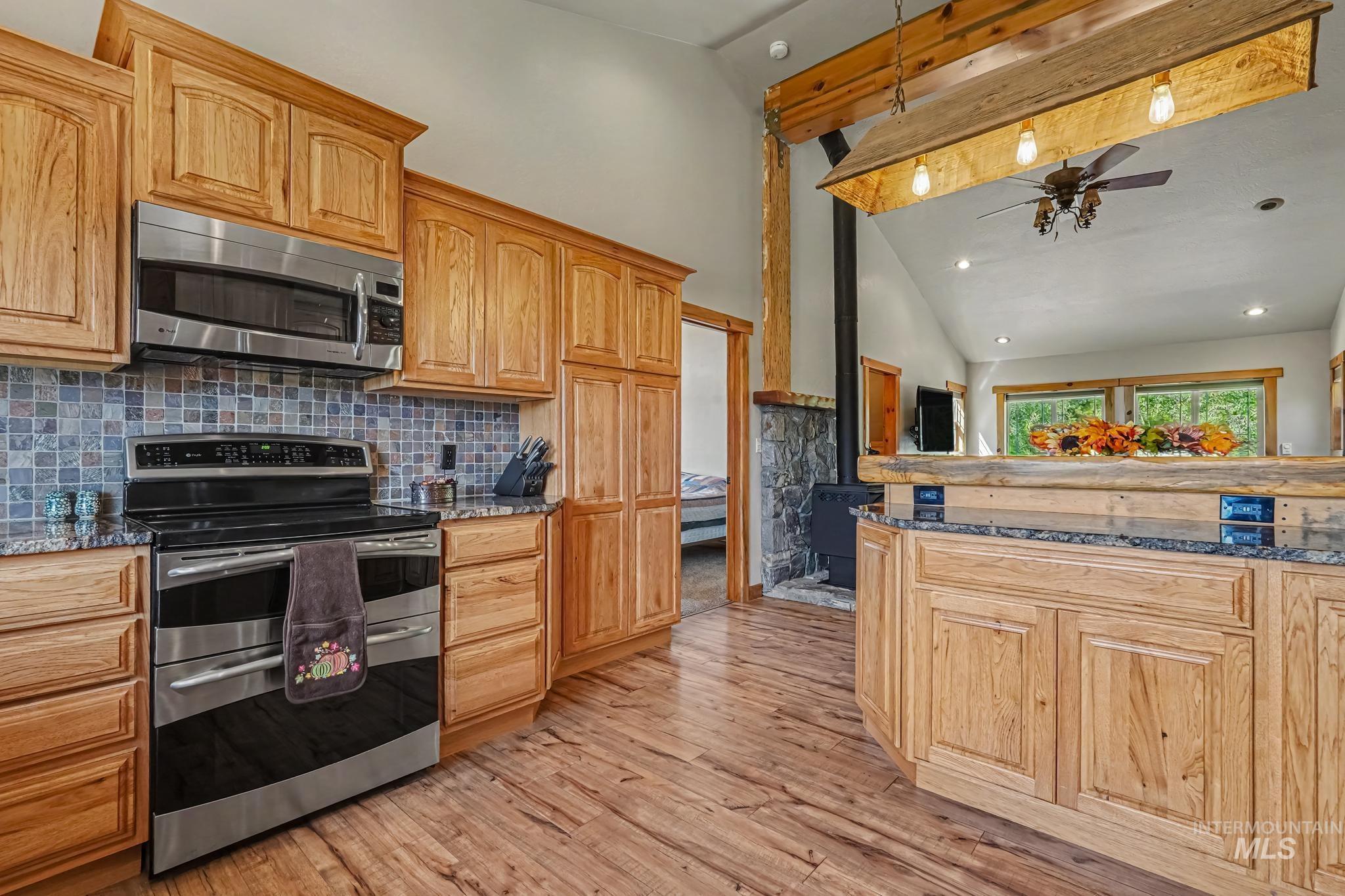 106 Wilderness Lake Road Cascade, ID 83611 - Photo 16 of 35 Kitchen featuring wood-finish flooring, stainless steel appliances, mosaic tile backsplash, wood cabinetry, and a wood-wrapped breakfast bar