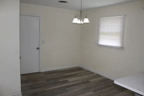an empty room with wooden floor chandelier and windows