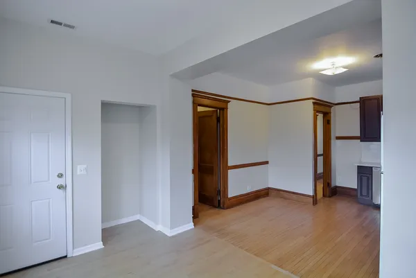 a view of an empty room with wooden floor and a kitchen