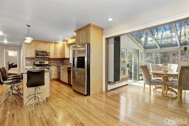 a kitchen with stainless steel appliances kitchen island granite countertop a refrigerator a stove a dining table and chairs with wooden floor