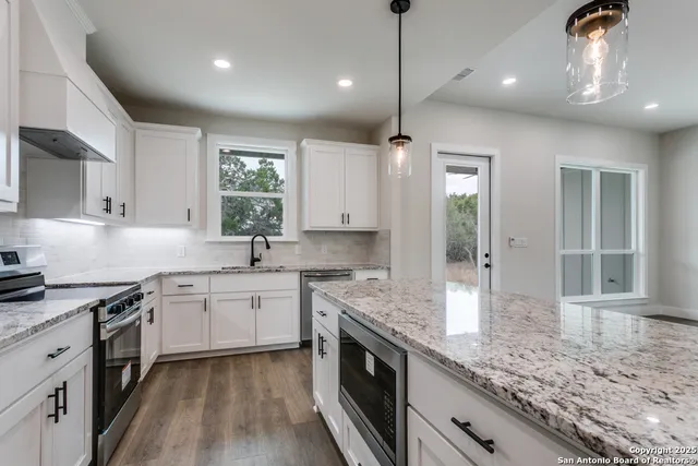 a kitchen with stainless steel appliances granite countertop stove a sink dishwasher a refrigerator and white cabinets with wooden floor