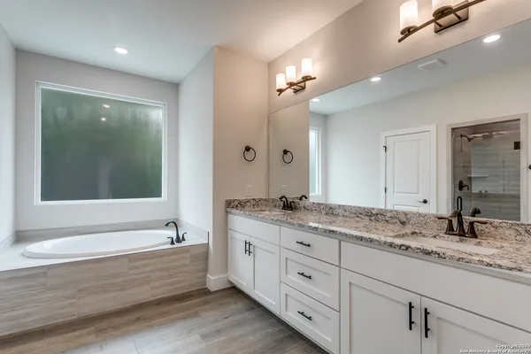 a bathroom with a granite countertop tub double vanity sink and mirrors