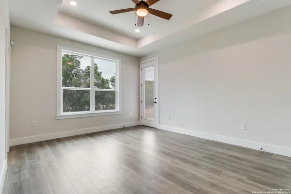 an empty room with wooden floor chandelier fan and windows