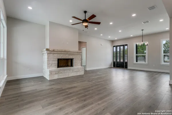 an empty room with wooden floor a fireplace a ceiling fan and windows