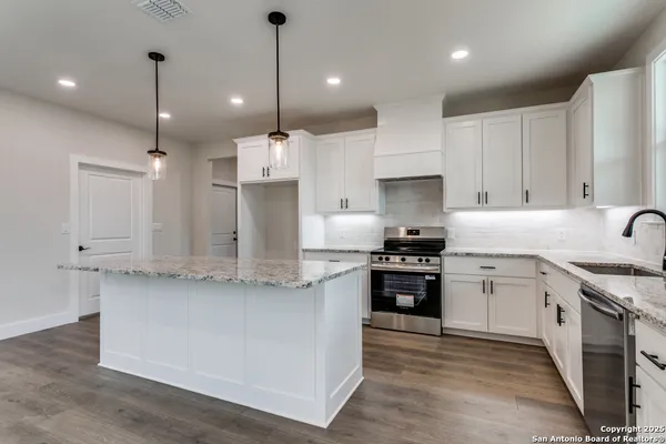 a large kitchen with stainless steel appliances granite countertop a stove a sink a refrigerator and white cabinets with wooden floor