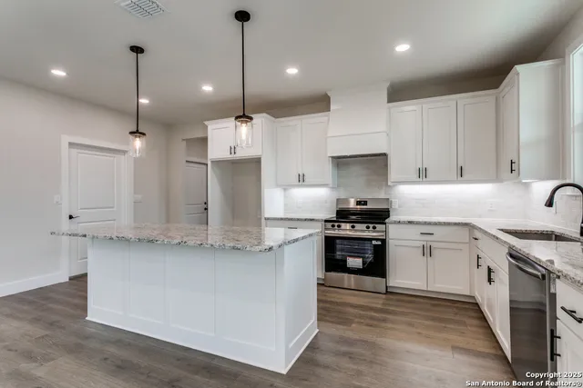 a large kitchen with stainless steel appliances granite countertop a stove a sink a refrigerator and white cabinets with wooden floor