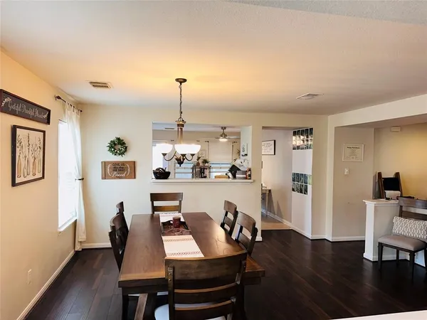 a dining room with furniture wooden floor kitchen view and a chandelier