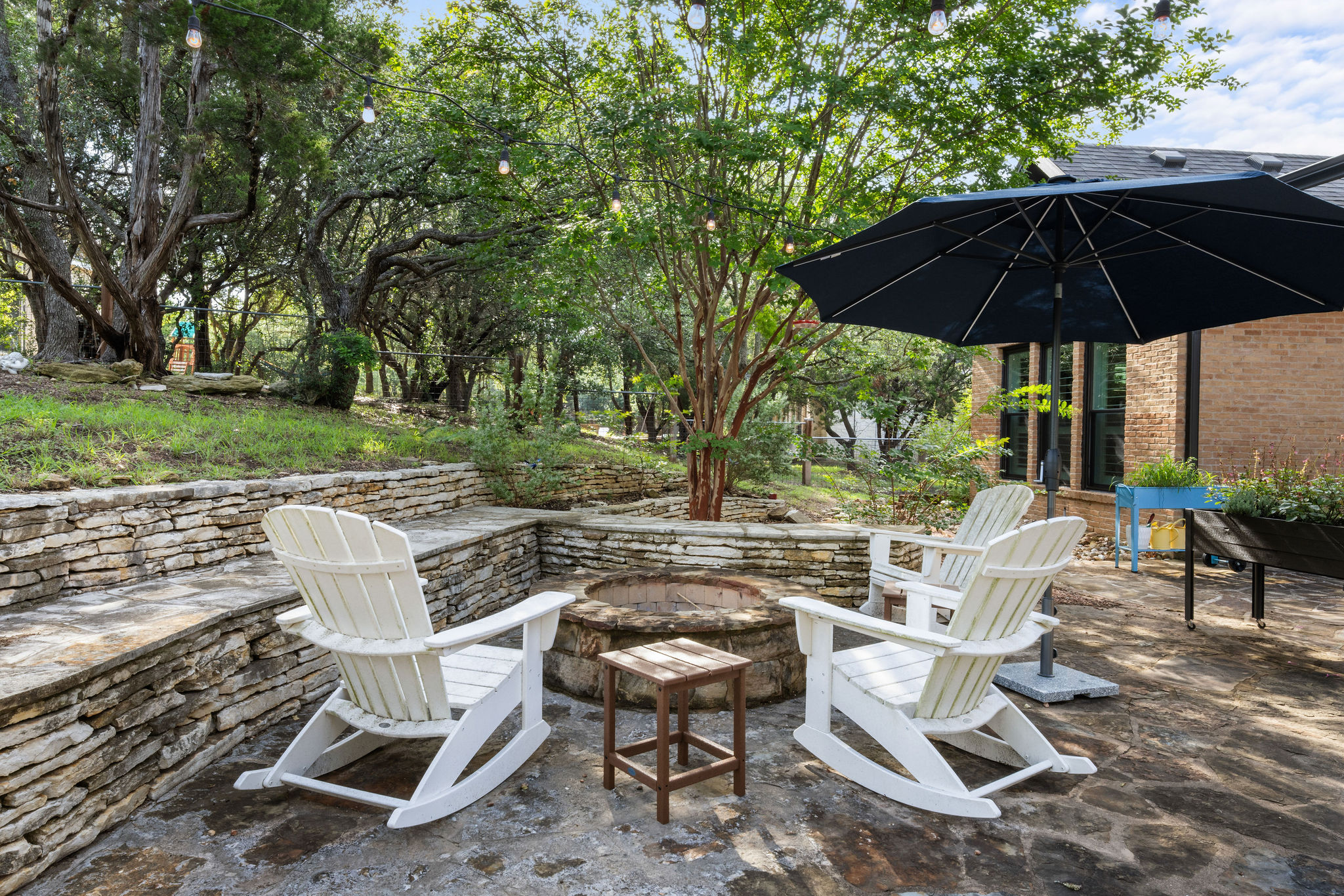 279 Rugged Earth Drive Austin, TX 78737 - Photo 36 of 39 An inviting stone patio with a built-in fire pit offers a serene outdoor retreat for relaxation and entertainment.