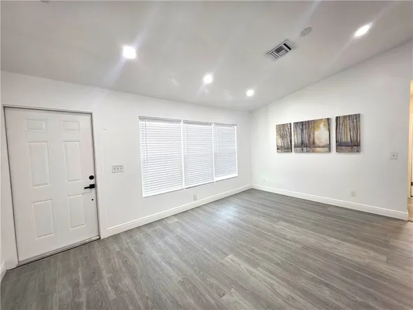 a view of an empty room with wooden floor and windows