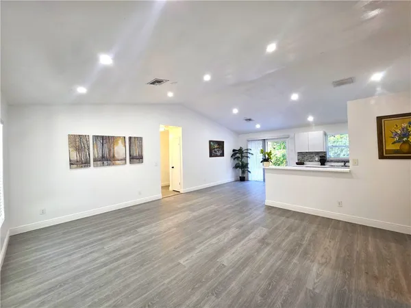 a view of an empty room with wooden floor and a kitchen