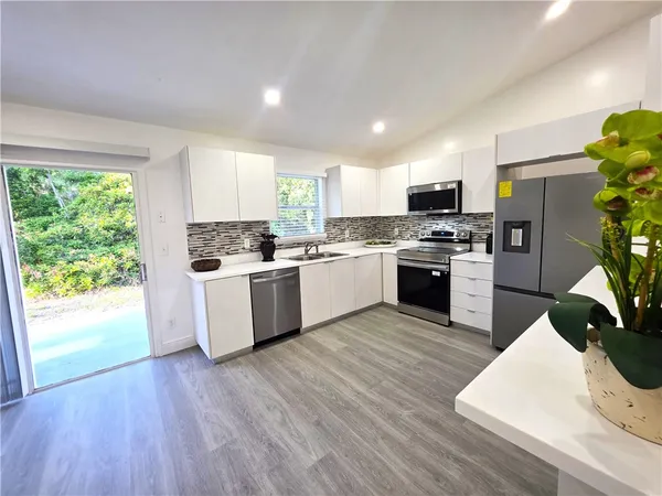 a kitchen with a white cabinets a sink a stove a refrigerator and a dining table with wooden floor