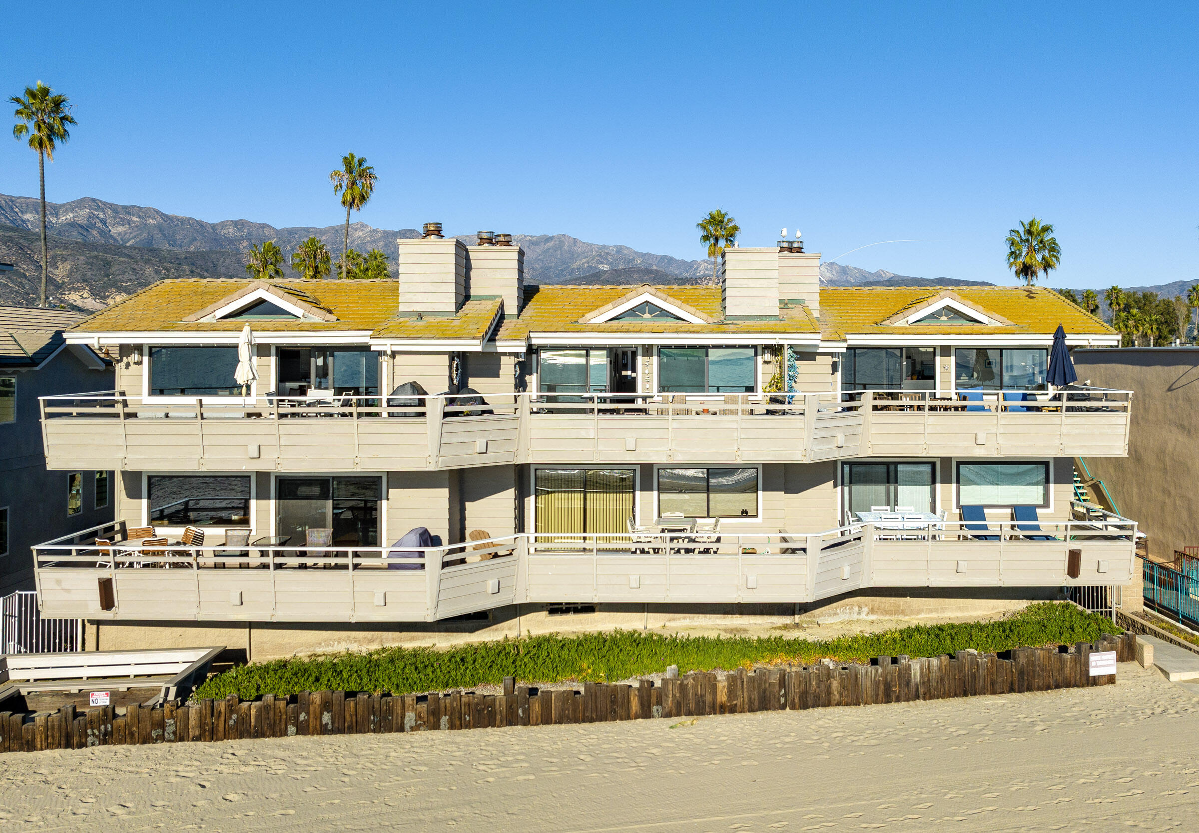 4925 Sandyland Road, Unit F Carpinteria, CA 93013 - Photo 5 of 6 a view of a white house with a swimming pool and lawn chairs under an umbrella