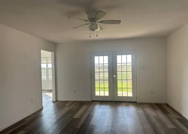 an empty room with wooden floor fan and windows