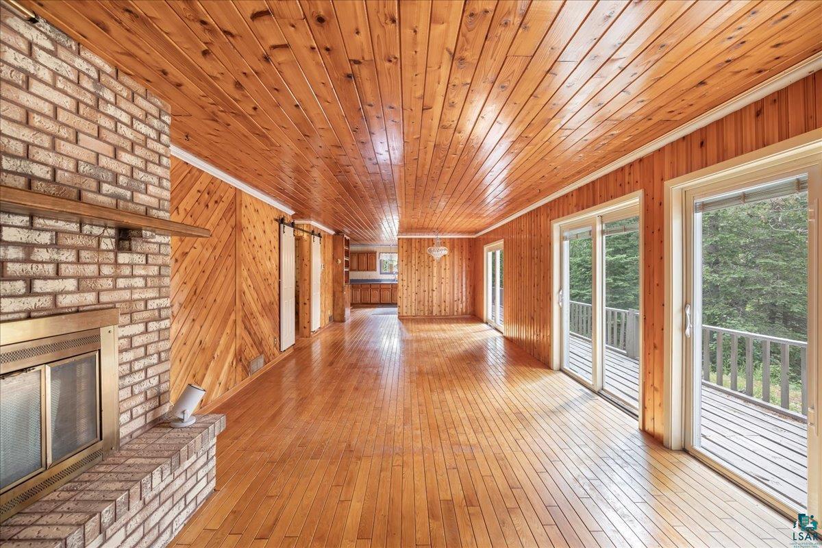 1804 North Bay Road Ely, MN 55731 - Photo 13 of 37 Unfurnished living room featuring wooden walls, a fireplace, light wood-type flooring, brick wall, and wooden ceiling