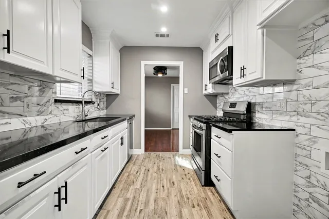 a kitchen with granite countertop a sink stainless steel appliances and white cabinets