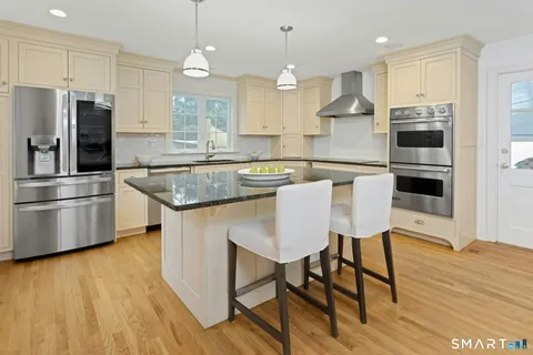 a kitchen with stainless steel appliances granite countertop a stove a refrigerator a kitchen island a dining table and chairs with wooden floor