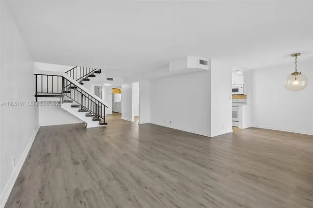 a view of an empty room with wooden floor and stairs