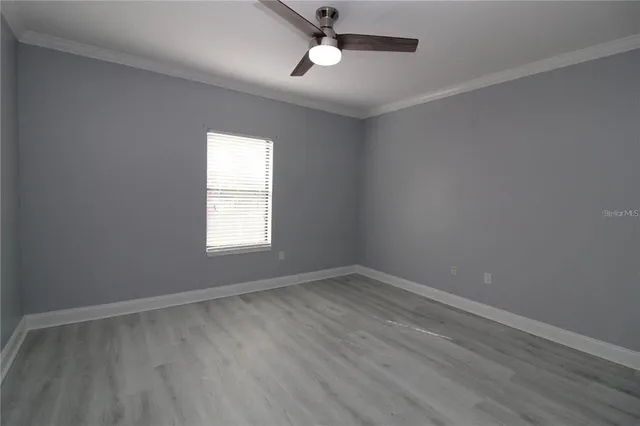 an empty room with wooden floor ceiling fan and windows
