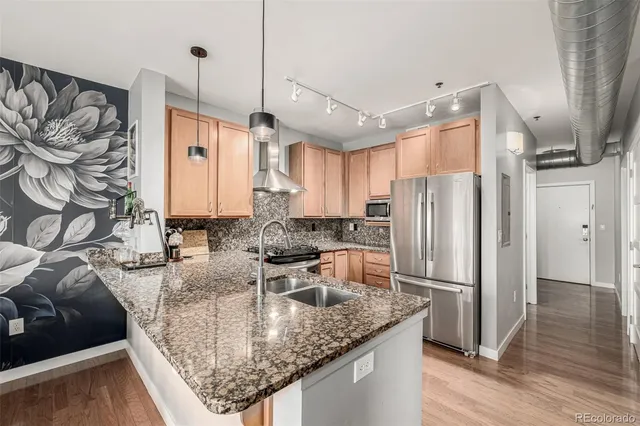 a kitchen with stainless steel appliances granite countertop a sink a refrigerator and a wooden floor