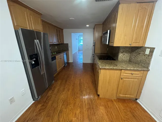 a kitchen with granite countertop wooden floors stainless steel appliances a sink and a window