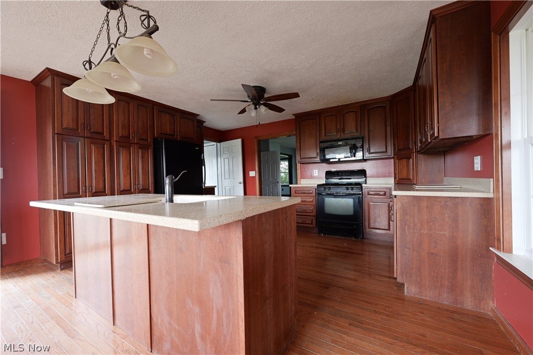 19105 Whitehead Road Lagrange, OH 44050 - Photo 18 of 37 Kitchen featuring ceiling fan, an island with sink, black appliances, hanging light fixtures, and wood-type flooring