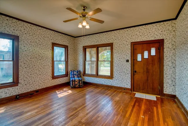a view of an empty room with wooden floor and a ceiling fan