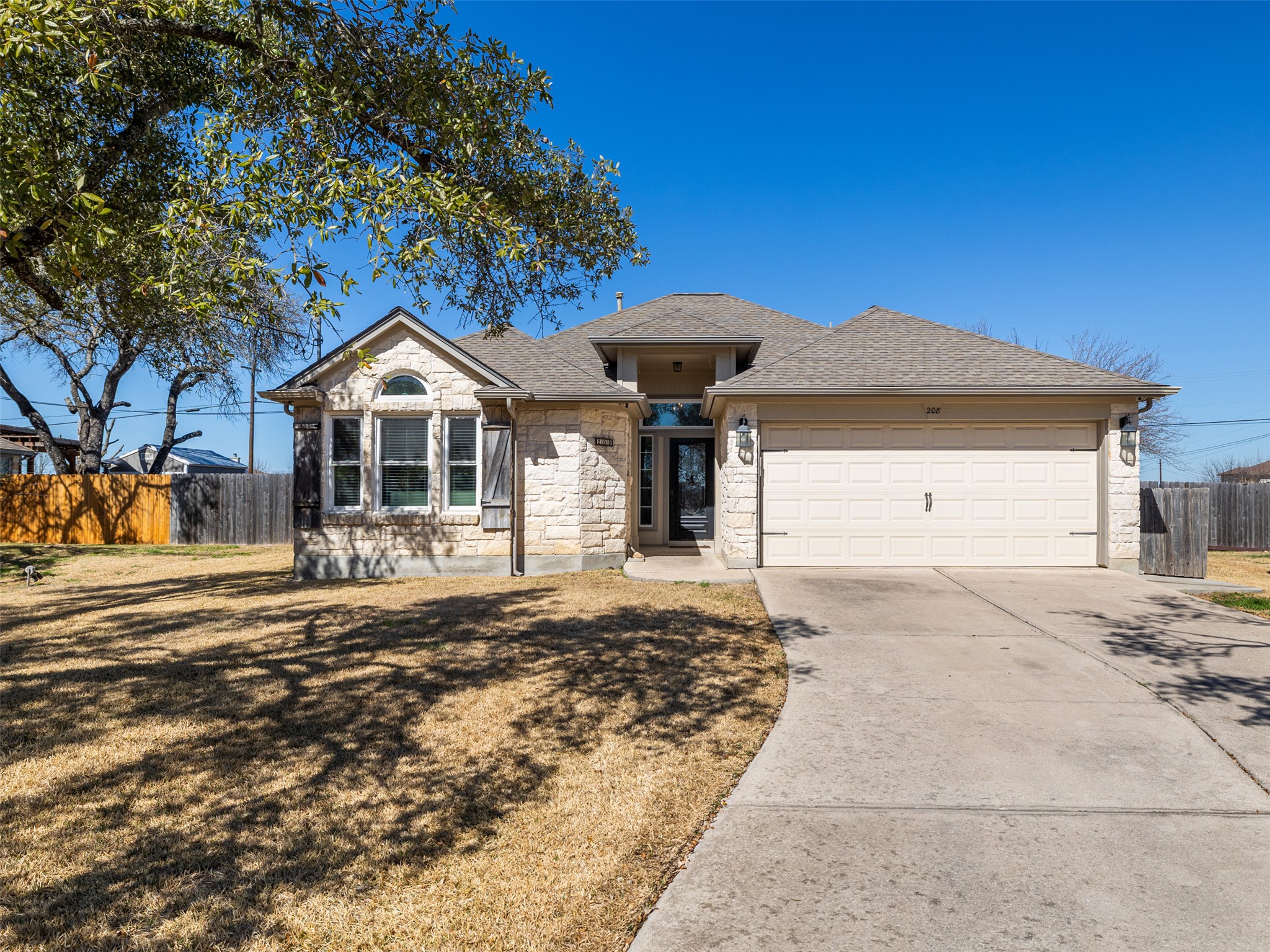 Ranch-style house with an attached garage, concrete driveway, stone siding, and roof with shingles