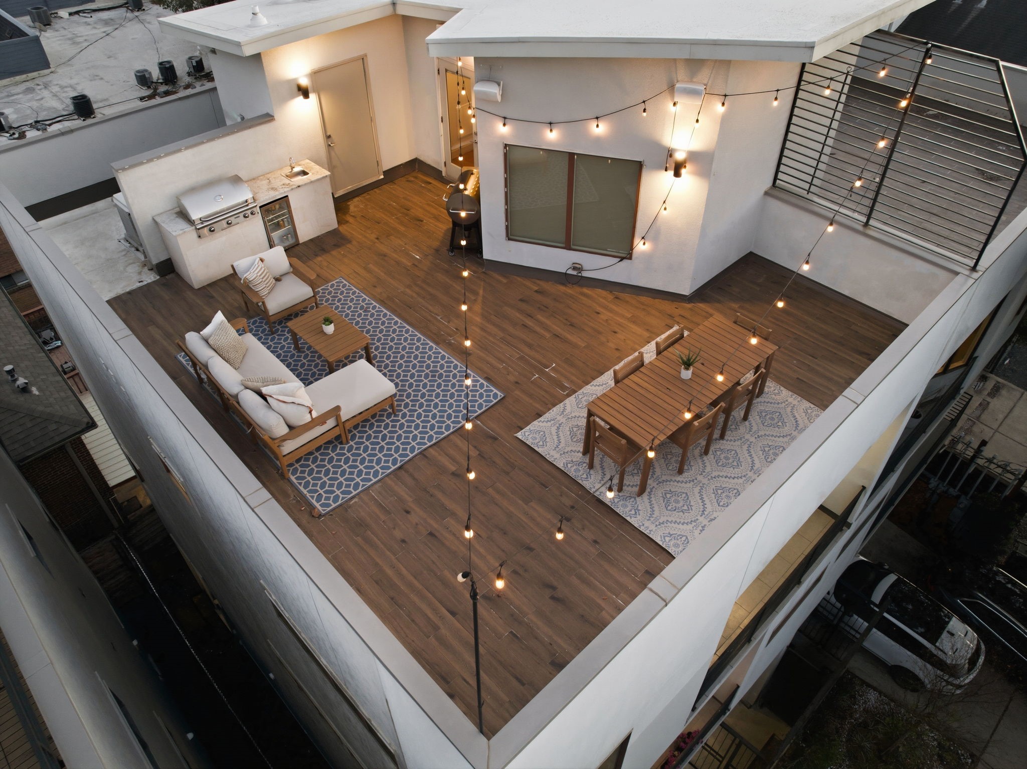 1405 Vermont Street, Unit A Houston, TX 77006 - Photo 5 of 46 Equipped with a high-end gas grill, sink, and beverage cooler, the gourmet summer kitchen serves as the ultimate hub for rooftop entertaining. String lights illuminate the expansive layout, highlighting distinct zones for alfresco dining and lounging across the low-maintenance wood-look flooring. This private outdoor retreat offers a sophisticated setting for hosting guests while enjoying the fresh air and open-sky views of the Bradford Mews community.