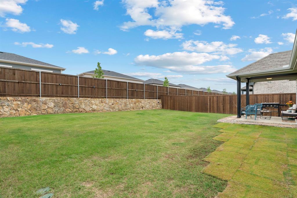 3112 Kingsgarden Road Denton, TX 76207 - Photo 37 of 38 Expansive backyard featuring a manicured lawn, a stone retaining wall, and a full privacy fence