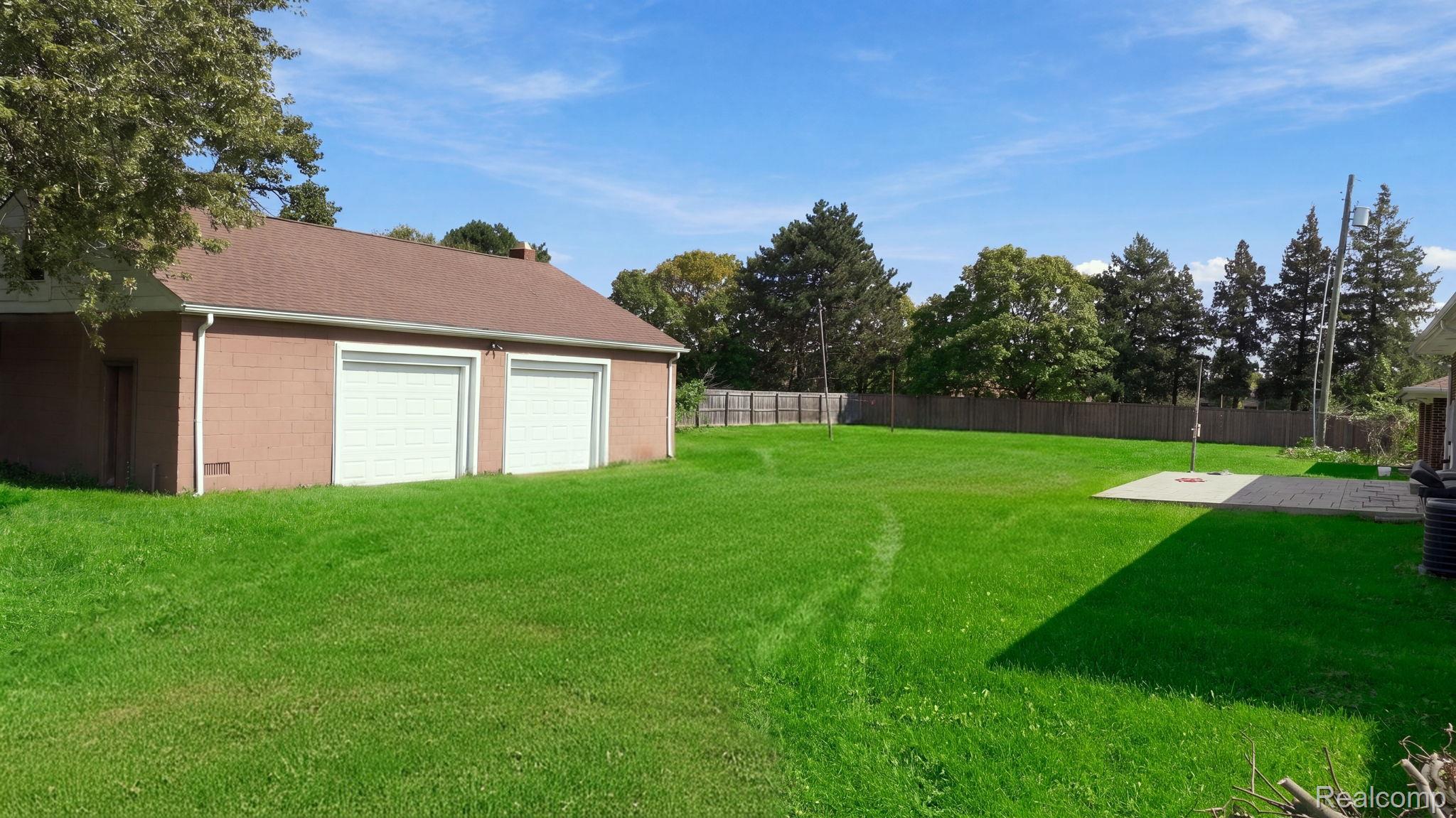5353 18 Mile Road Sterling Heights, MI 48314 - Photo 38 of 53 Expansive green lawn with a two-car garage featuring white overhead doors, a paved patio area, and perimeter fencing