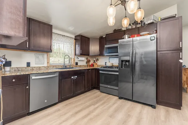 a kitchen with stainless steel appliances granite countertop a refrigerator a sink dishwasher a stove and a dining table with wooden floor