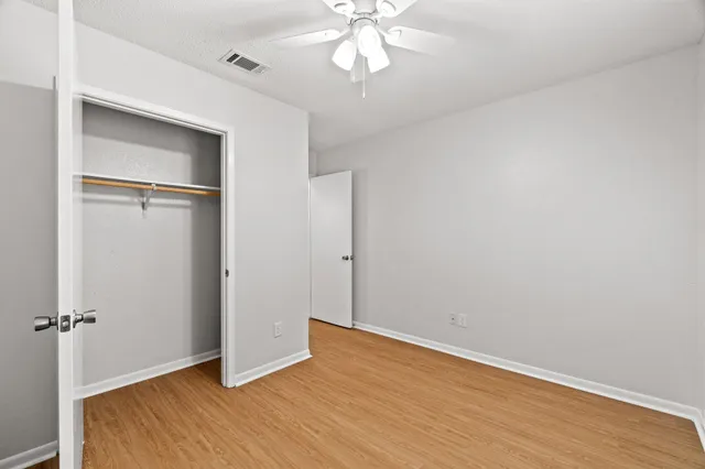 an empty room with wooden floor closet and windows