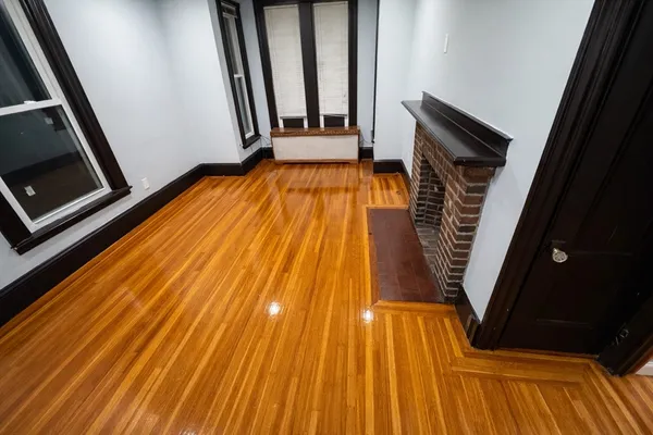 a view of an empty room with wooden floor and a fireplace