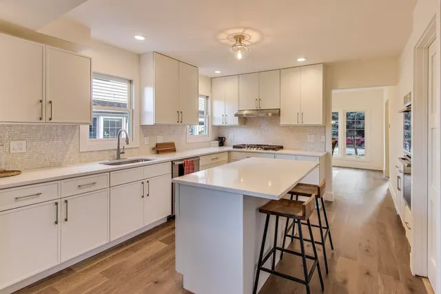 a kitchen with stainless steel appliances granite countertop a sink a stove a refrigerator and white cabinets with wooden floor