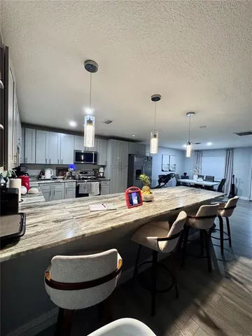 a kitchen with stainless steel appliances granite countertop a dining table chairs and a refrigerator