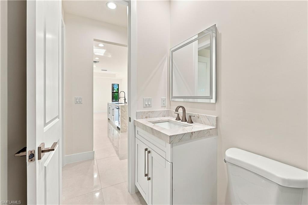 183 5th Street Southwest Naples, FL 34117 - Photo 23 of 40 White vanity with integrated sink, stone countertop, bronze-finish faucet, and an illuminated mirror
