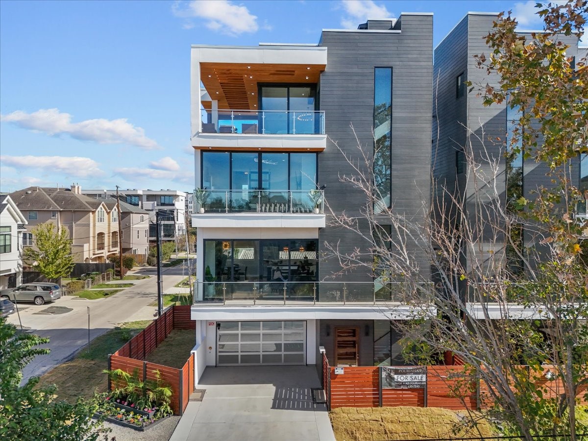 516 Reinerman Street Houston, TX 77007 - Photo 3 of 42 Modern three-story townhouse with sleek, dark exterior and large glass windows. Features spacious balconies and a covered garage. Situated on a corner lot with a fenced yard, in a residential neighborhood.