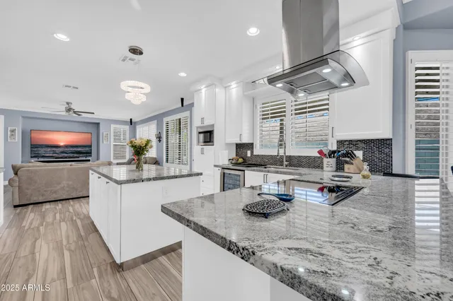 a kitchen with stainless steel appliances kitchen island granite countertop a refrigerator a stove and white cabinets with wooden floor