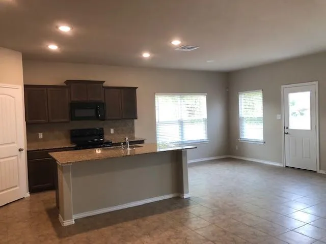 a kitchen with stainless steel appliances a sink a stove a microwave a refrigerator a window and cabinets