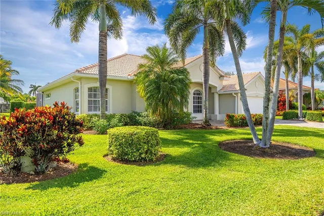 a front view of yellow house with a small yard and palm trees