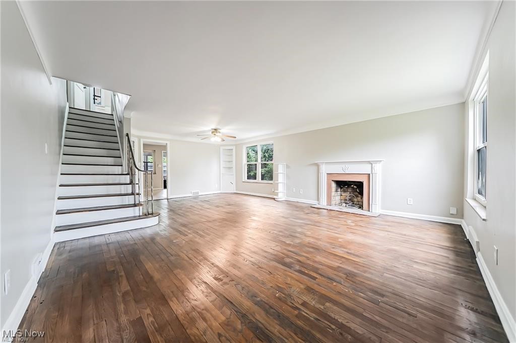 3837 Mayfield Road Cleveland, OH 44121 - Photo 11 of 29 Unfurnished living room with stairway, a fireplace with raised hearth, dark wood-style flooring, and a ceiling fan