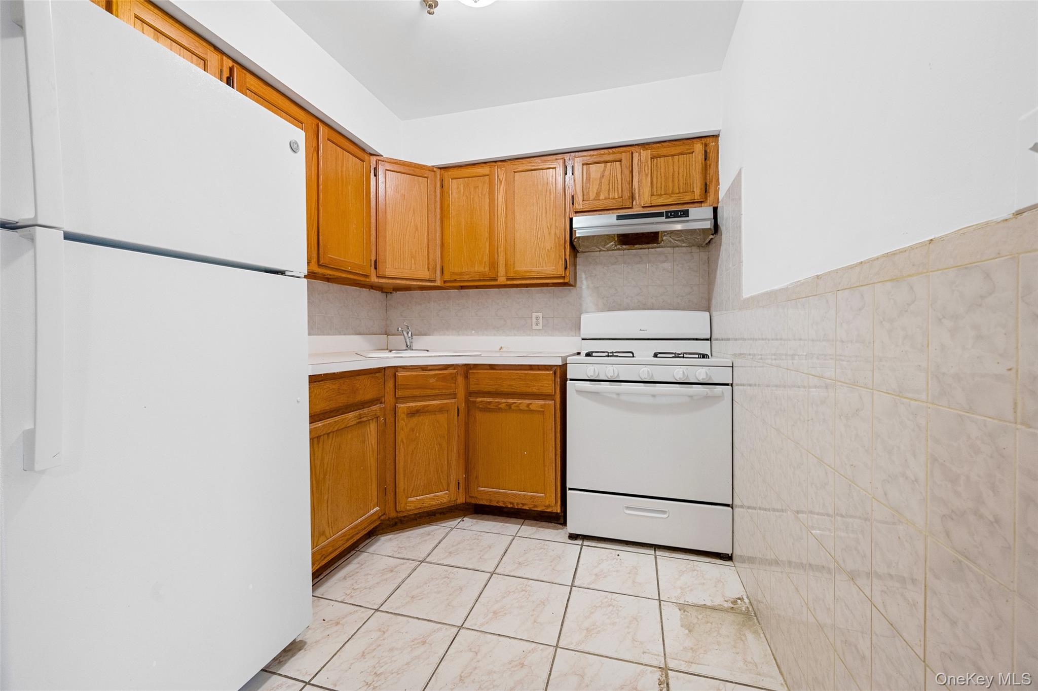 108-10 35th Avenue Queens, NY 11368 - Photo 16 of 29 Kitchen featuring white appliances, light countertops, brown cabinets, under cabinet range hood, and decorative backsplash