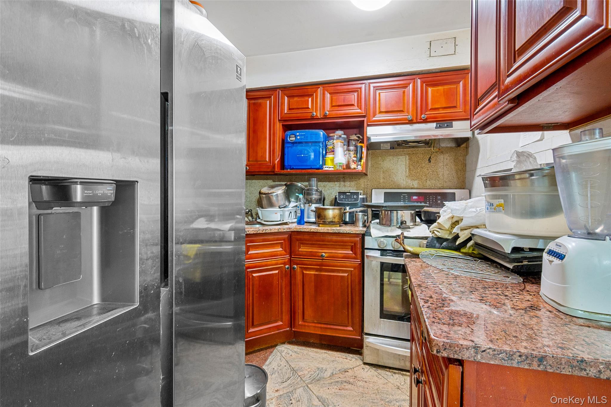 108-10 35th Avenue Queens, NY 11368 - Photo 24 of 29 Kitchen featuring stainless steel appliances, under cabinet range hood, reddish brown cabinets, and light stone counters